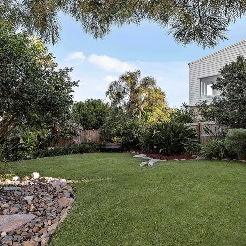 Backyard lawn bordered by garden beds and stone