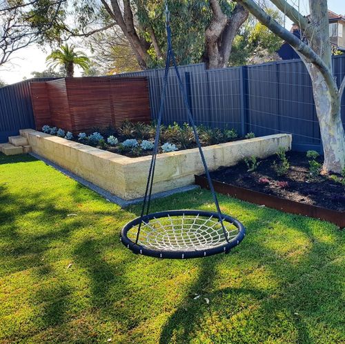 Shaded backyard lawn with a swing and limestone edging